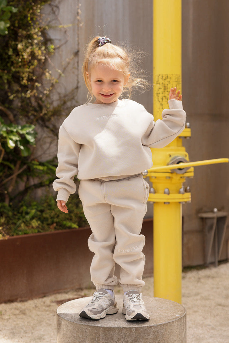 Child wearing the Remy & Co. Beige crewneck sweatshirt and matching joggers in front of a yellow pole at a playground.