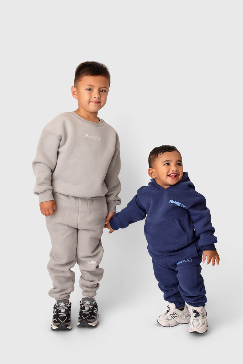Two children wearing Remy & Co. tracksuit sets in Dark Grey and Navy against light grey background.