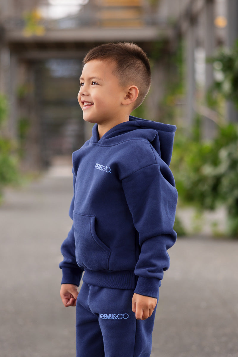 Side view of child wearing the Remy & Co. Navy Blue Puff Print Hoodie Tracksuit Set outdoors.