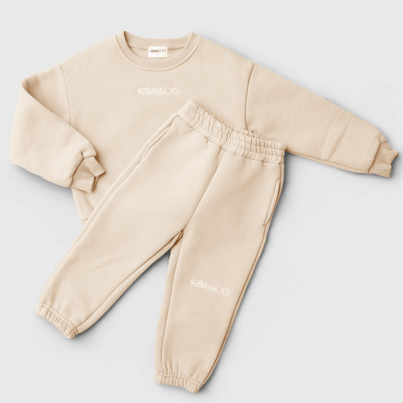 Remy & Co. Beige kids embroidered crewneck tracksuit set with matching joggers on a light grey background.