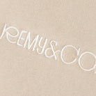 Close-up of the Remy & Co. embroidered logo on Beige coloured fabric.