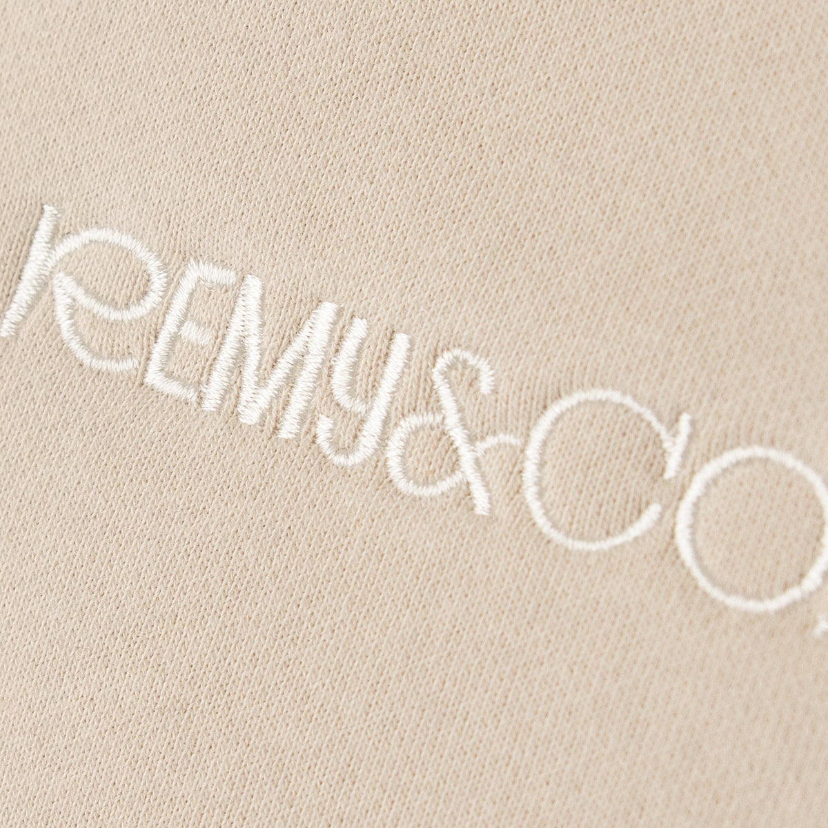 Close-up of the Remy & Co. embroidered logo on Beige coloured fabric.