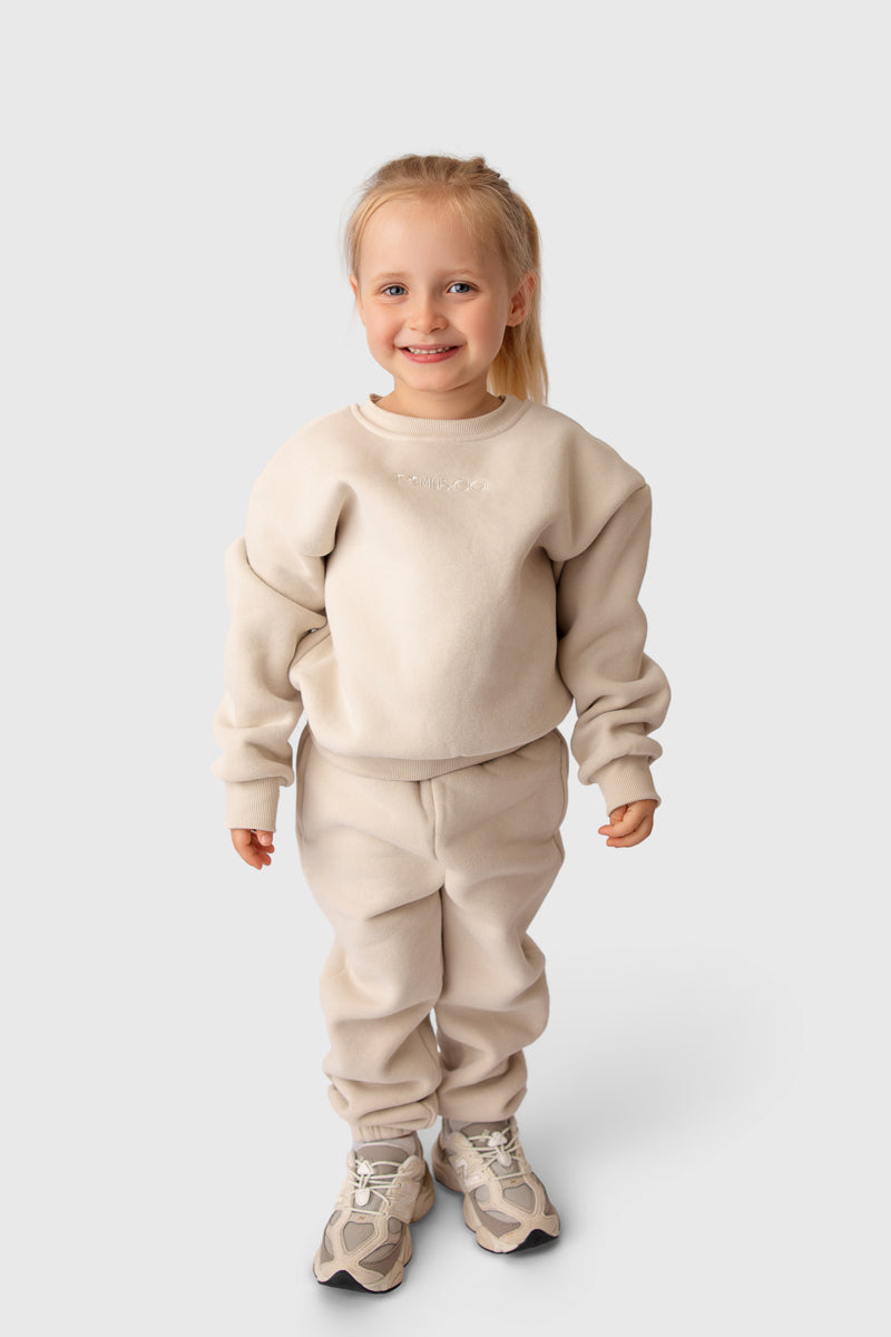Full-length studio image of a child wearing the Remy & Co. Beige crewneck sweatshirt and matching joggers.
