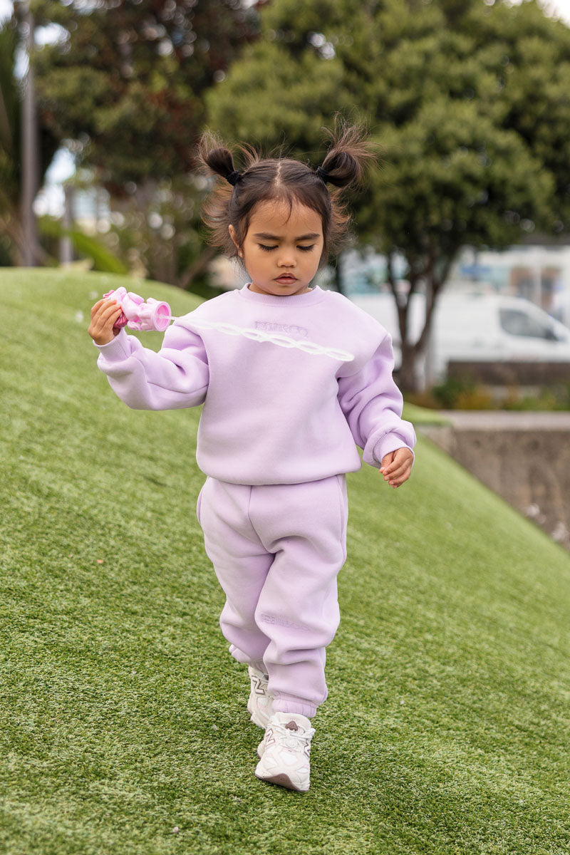 Child wearing the Remy & Co. Lilac crewneck sweatshirt and matching joggers while playing with a bubble wand on grass.
