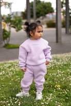 Child wearing the Remy & Co. Lilac crewneck sweatshirt and matching joggers among flowers