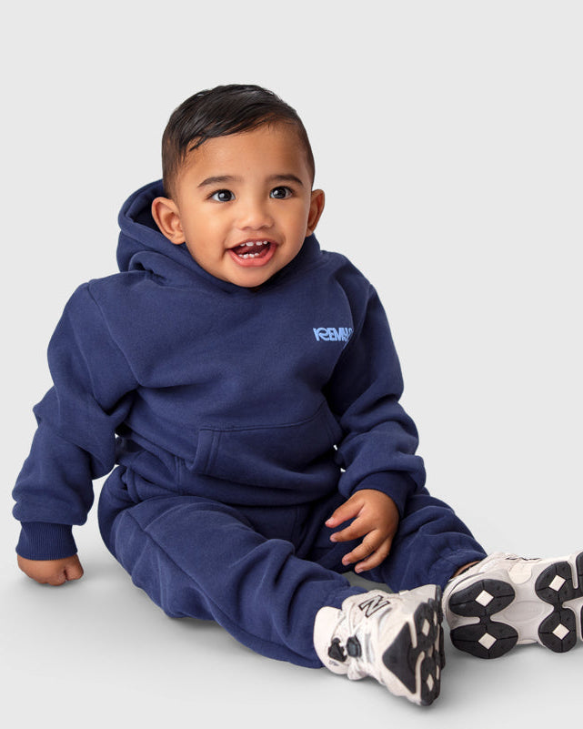 Child sitting in a studio wearing the Remy & Co. Navy Blue Puff Print Hoodie Tracksuit Set.
