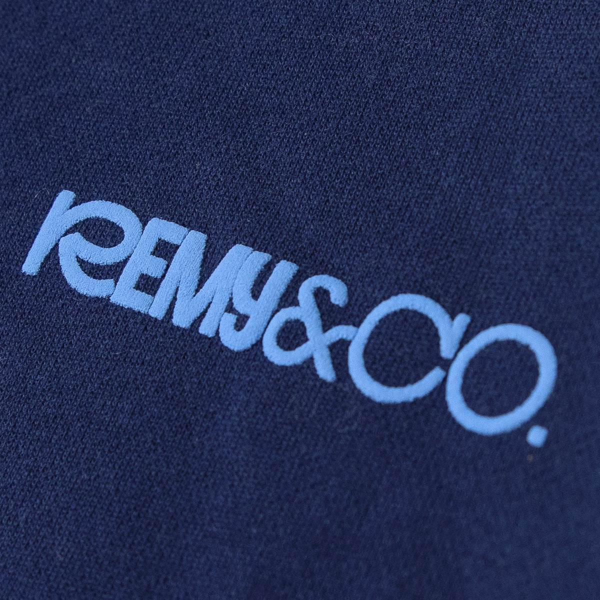Close-up of the Remy & Co. sky blue puff print logo on Navy Blue coloured fabric.