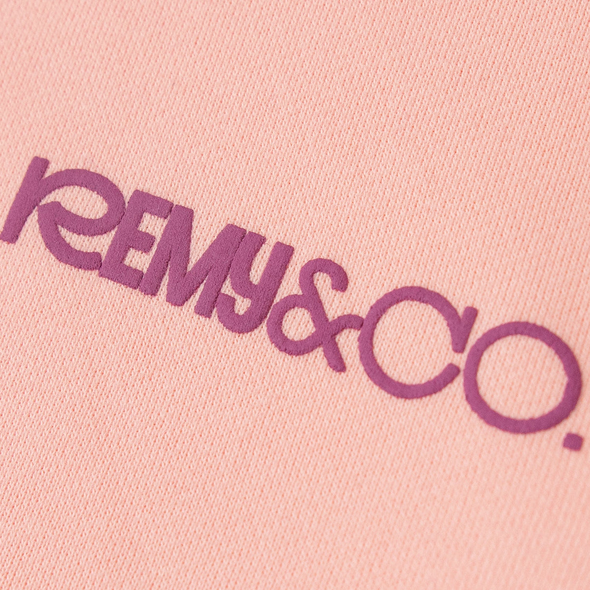 Close-up of the Remy & Co. puff print logo on Pink coloured fabric.